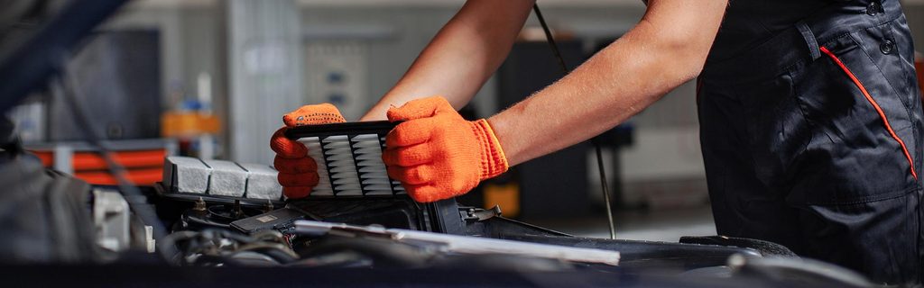 Automotive technician replacing a vehicle air filter under the hood during maintenance service.
