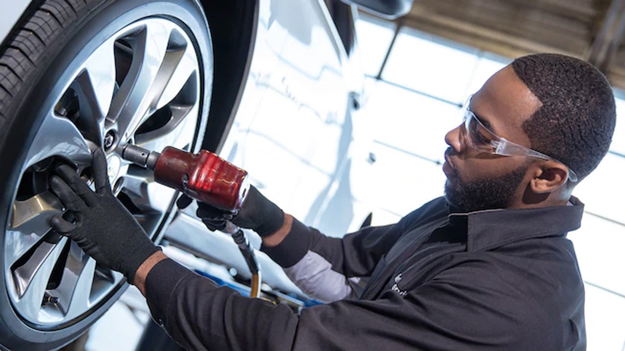 A mechanic using a pneumatic impact wrench to remove a car wheel.