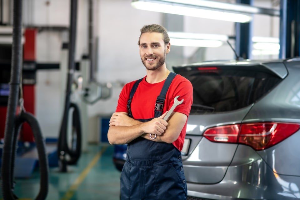 Smiling mechanic in overalls holding a wrench in an auto repair shop.