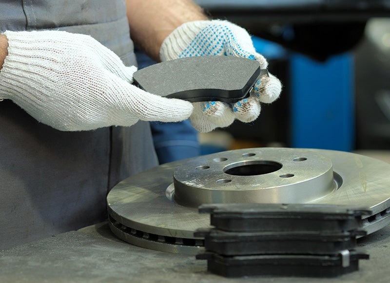 Gloved hands holding a new brake pad over a brake rotor