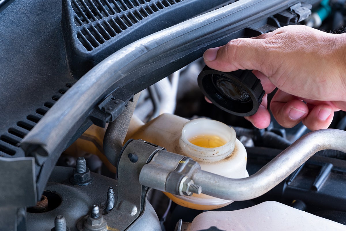 A hand opening the cap of a vehicle's brake fluid reservoir