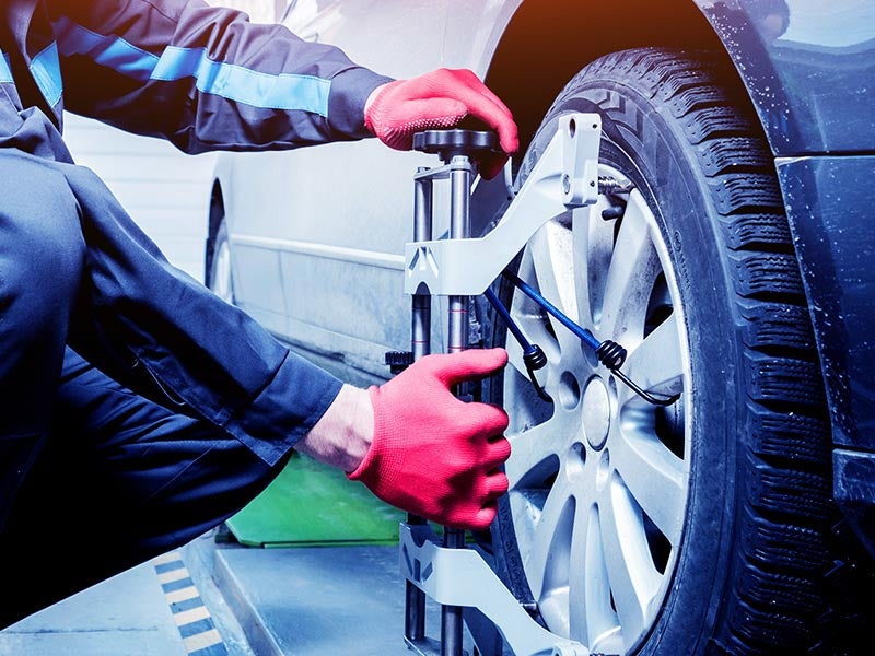 A mechanic in red gloves attaches a wheel alignment tool to a car.
